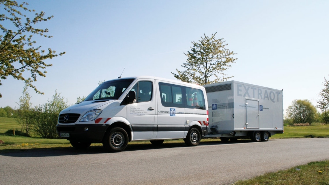 Ein Lieferwagen mit der Aufschrift „Happan Aircraft“, der oft mit der Rohrreinigung beauftragt wird, zieht einen Anhänger mit der Aufschrift „EXTRAQT“ auf einer von Bäumen gesäumten Straße.