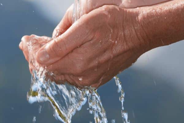 Nahaufnahme von hohlen Händen, die vor einem verschwommenen blauen Hintergrund fließendes Wasser auffangen und halten. Sie symbolisieren die Reinheit und Effizienz, die bei kommunalen Rohrreinigungsprozessen oft angestrebt wird.