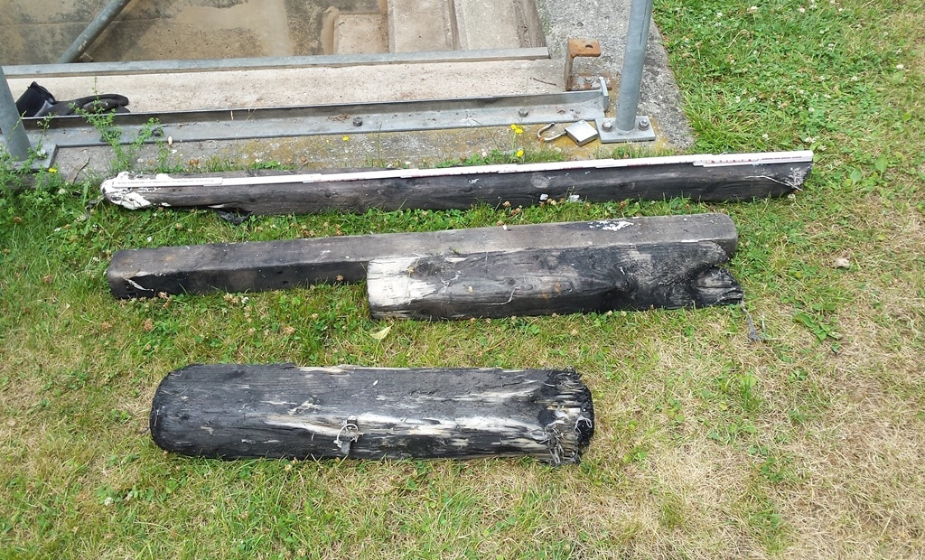 Three partially burnt wooden beams lying on grass near a concrete structure.