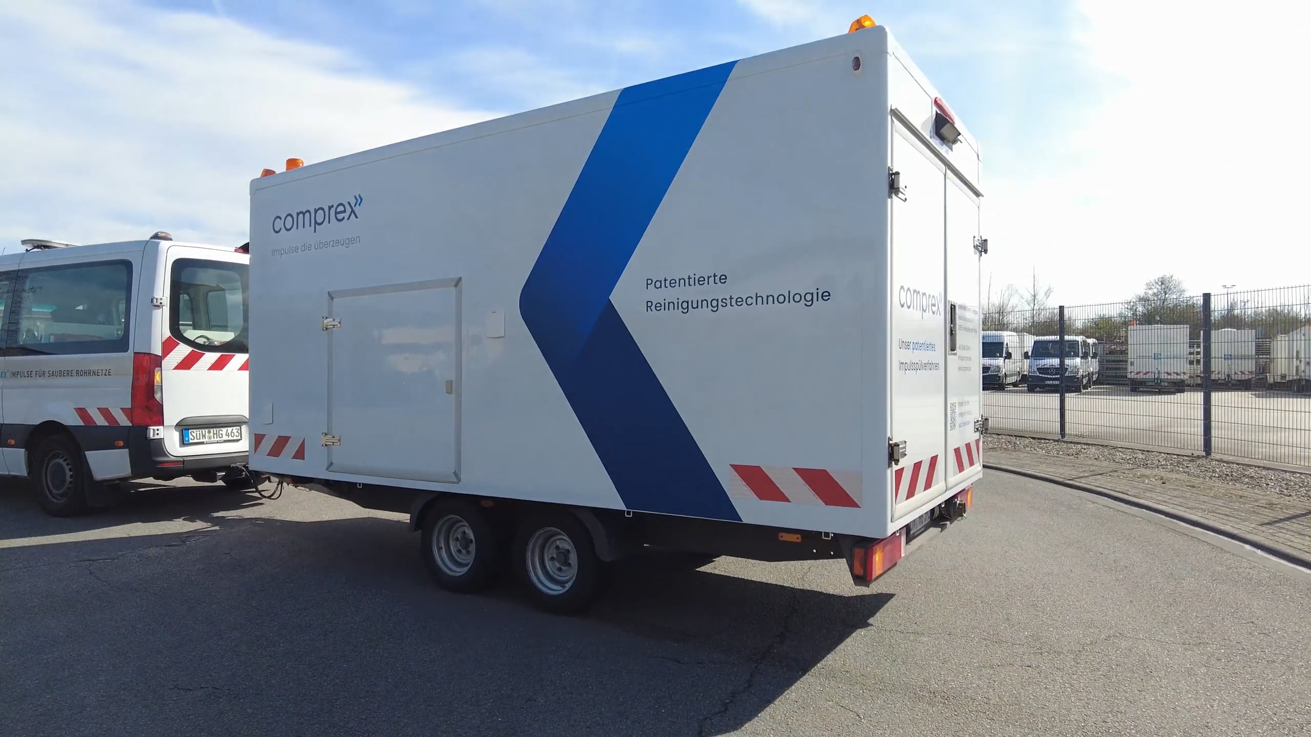 Weißer Anhänger mit Aufschrift „Comprex® patentierte Reinigungstechnologie“, geparkt auf einer Asphaltfläche, blauer Himmel über ihm, demonstriert fortschrittliche Rohrleitungs- und Anlagenreinigung mit Comprex®.