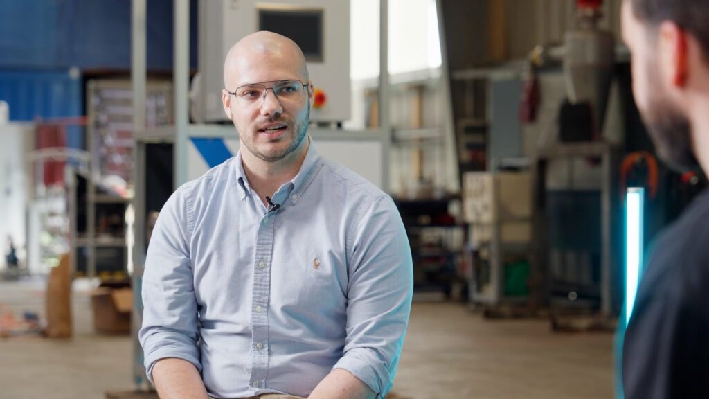 Ein Mann im blauen Hemd sitzt in einer industriellen Umgebung und diskutiert in vollem Gespräch über die Vorteile der Rohrleitungs- und Anlagenreinigung mit Comprex®.